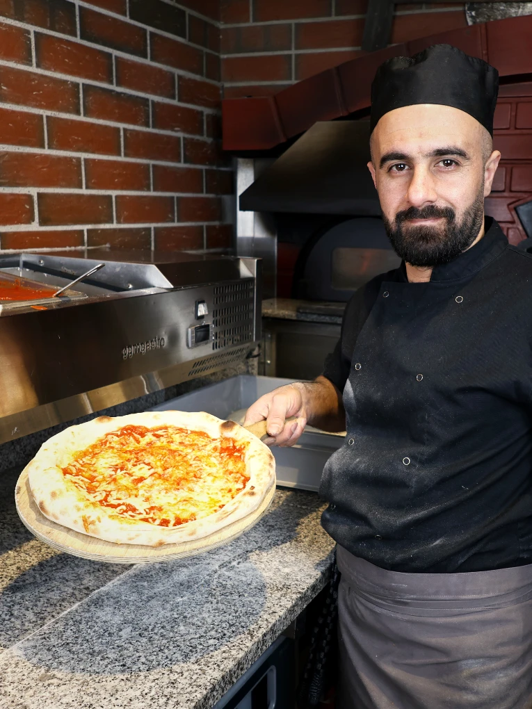 Pizzabäcker zeigt Pizza frisch aus dem Ofen heraus